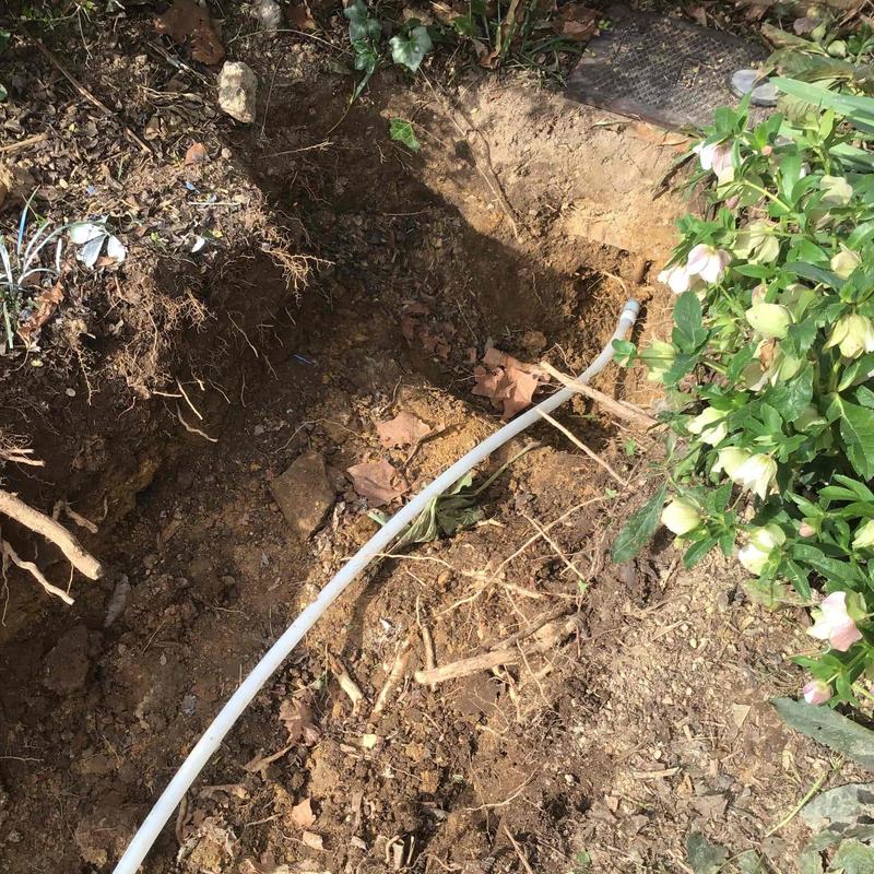 Water line installation trench with white pipe and foliage