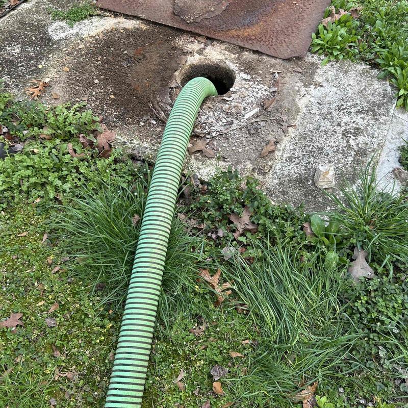 Septic tank inlet with green suction hose in grass