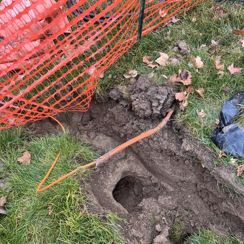 Main water line excavation with orange caution fencing