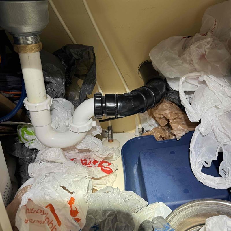 Sink drain pipes with PVC and black fittings under cluttered cabinet