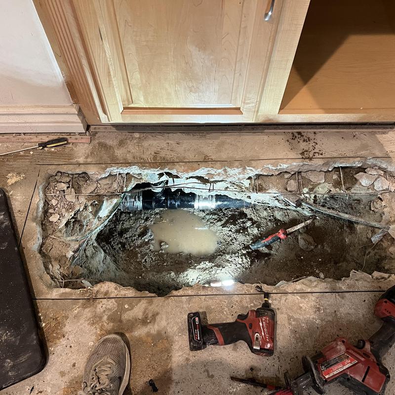 Sewer pipe exposed under concrete floor with tools nearby