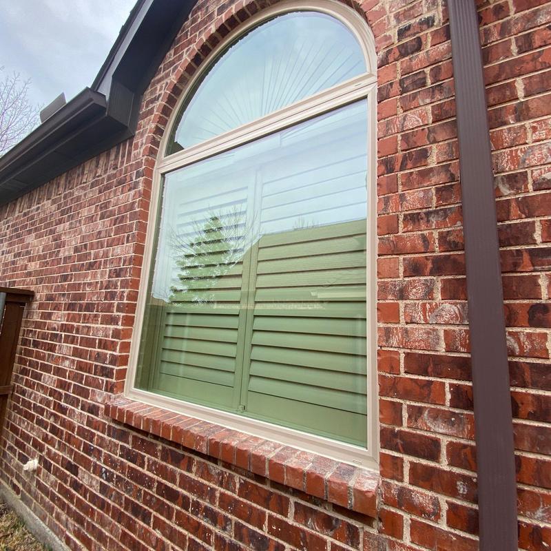 Almond vinyl arched window installation on brick wall