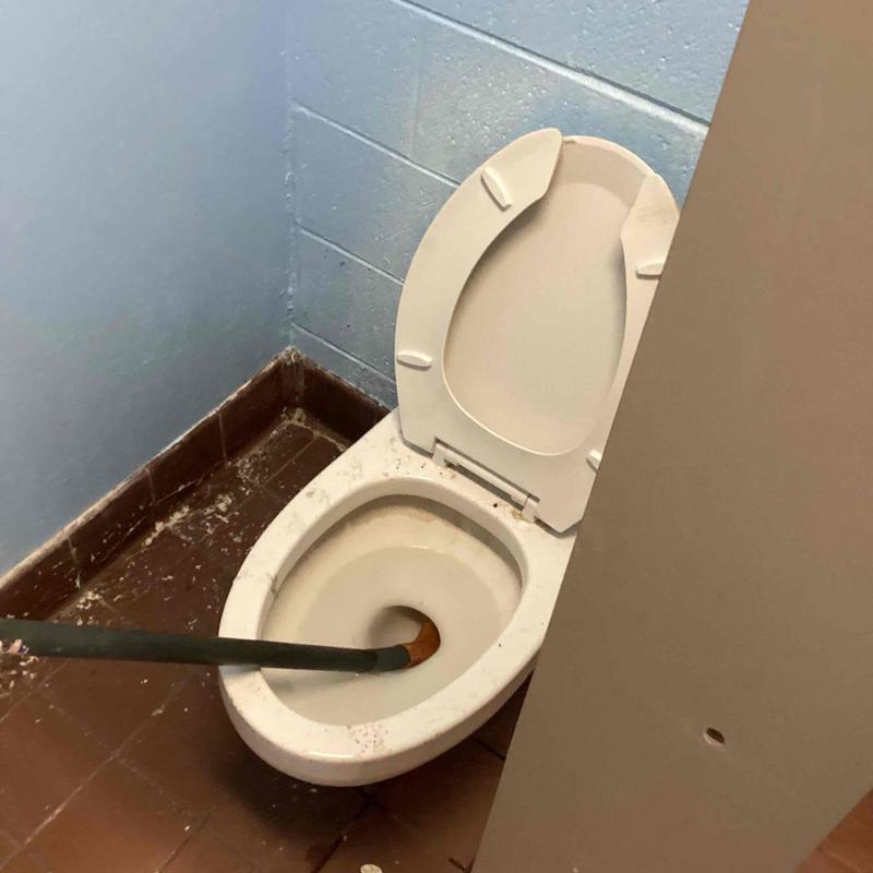 Toilet bowl with auger cable in stall corner