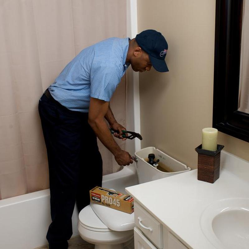 Toilet tank repair with plumber using wrench in bathroom