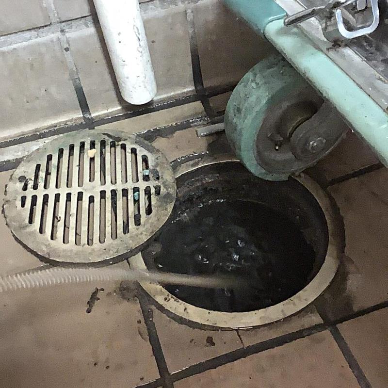 Kitchen floor drain with removed grate and hose inserted