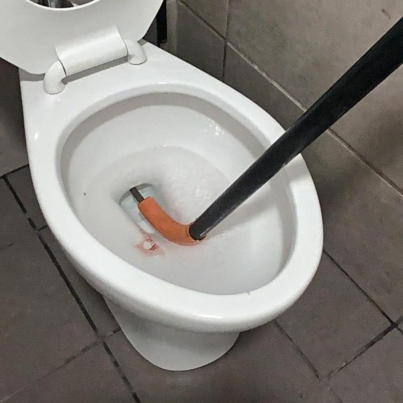 Toilet auger clearing clog in commode bowl