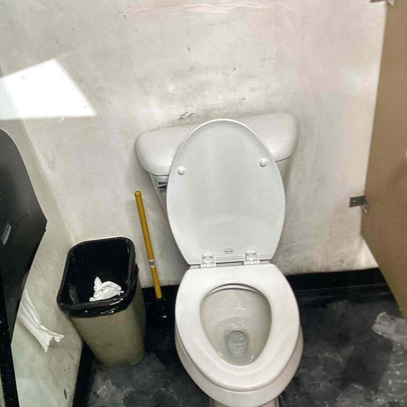 Toilet with open lid and trash can nearby