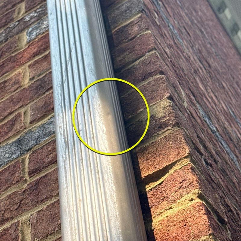 Downspout metal dent with rust on brick wall