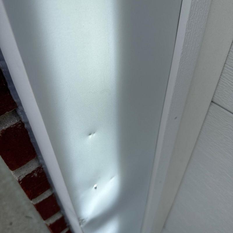 Vinyl siding with hail damage dents near brick wall