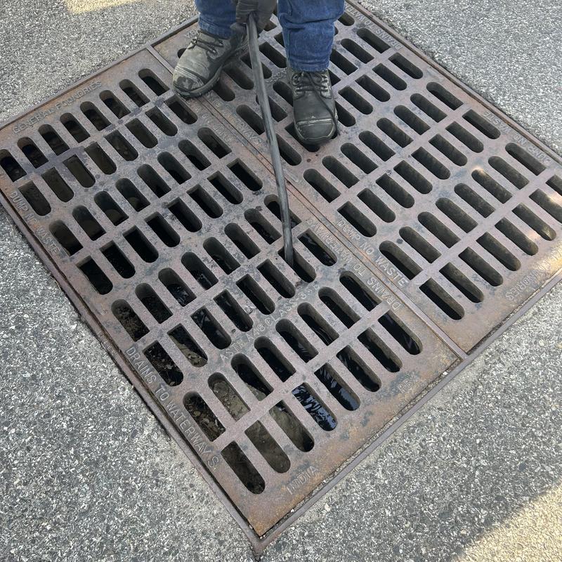 Storm drain cleaning with rod tool on asphalt surface Storm drain cleaning with rod tool on asphalt surface