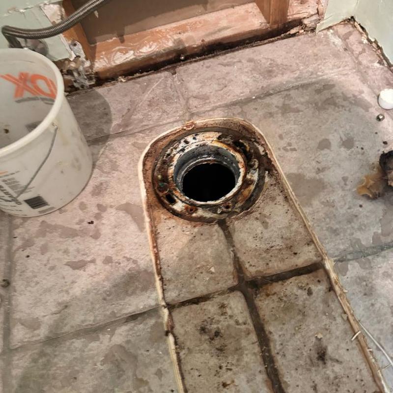Toilet flange with rust and water damage on tile floor Toilet flange with rust and water damage on tile floor