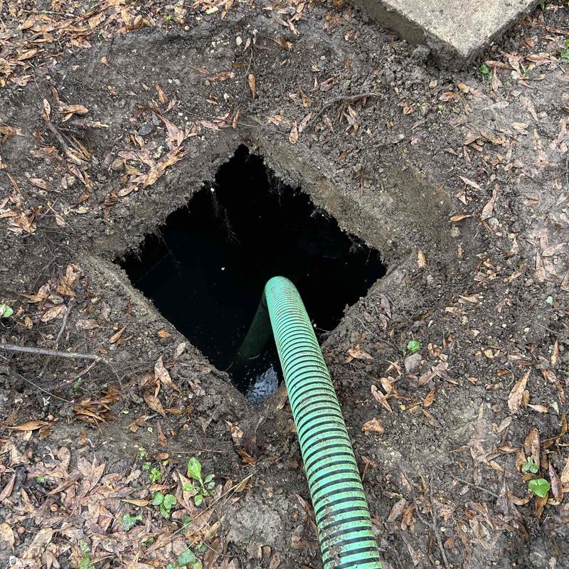 Septic tank with green pump hose in soil opening