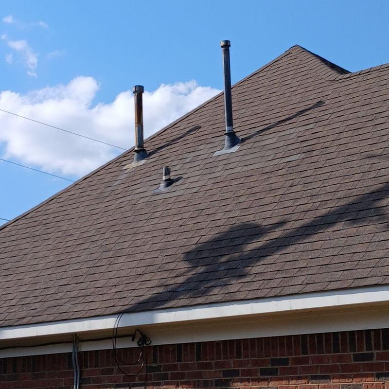 Asphalt shingle roof with vent pipes under clear sky