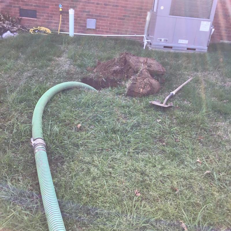 Septic tank excavation with green hose and shovel nearby
