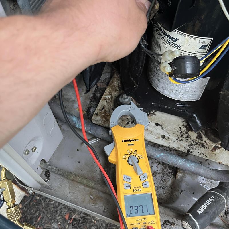 Carrier AC compressor with clamp meter and technician hand