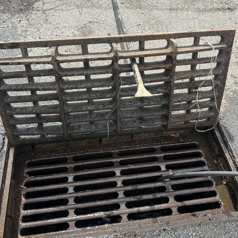 Outdoor storm drain grate and cleaning hose in open drain Outdoor storm drain grate and cleaning hose in open drain