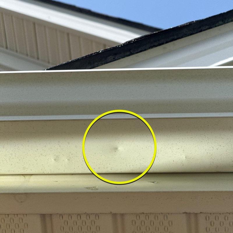 Gutter dent with yellow inspection circle on fascia board