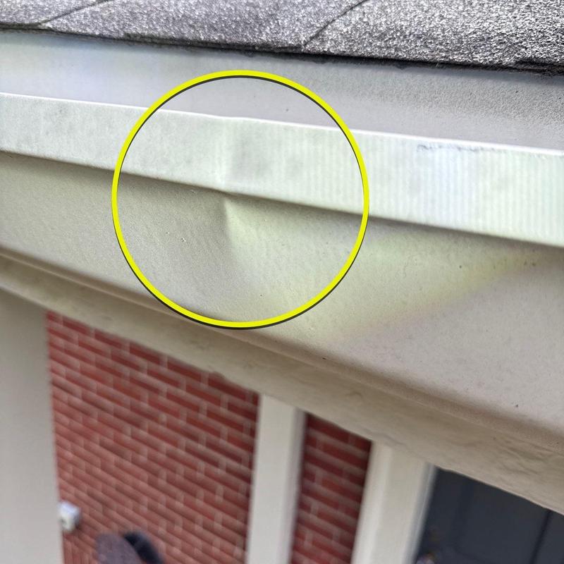 Gutter dent damage highlighted on white eavestrough