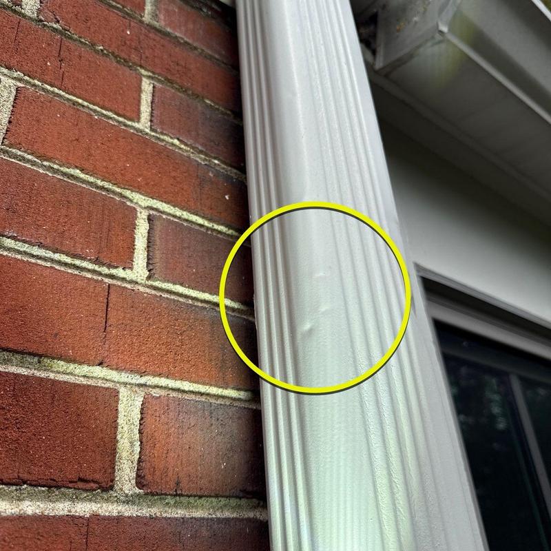 Vinyl downspout dent near brick wall closeup