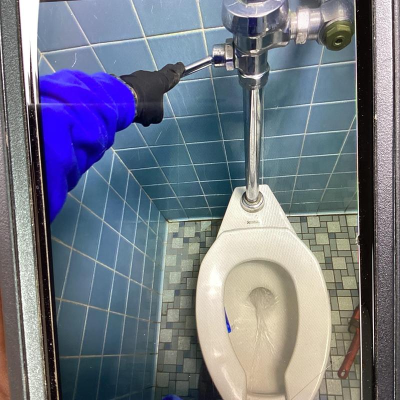 Urinal flush valve adjustment with wrench in blue tile restroom