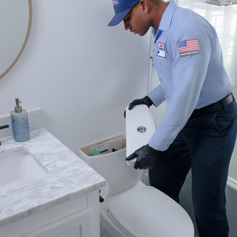 Toilet tank inspection by plumber in bathroom