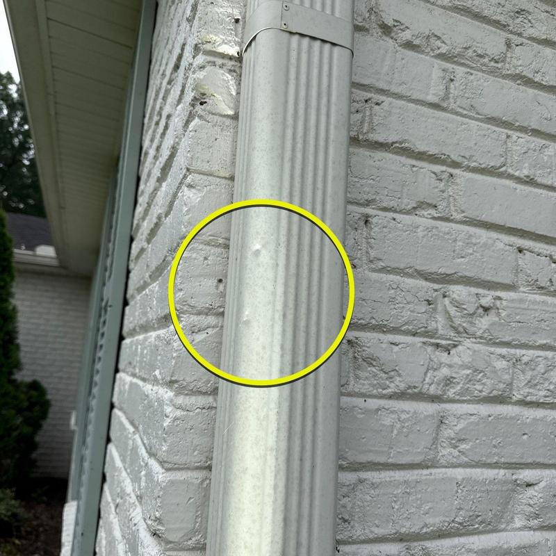 Metal downspout with hail dents on brick wall exterior