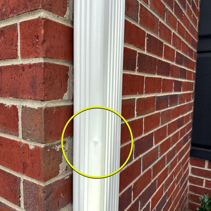 Downspout dent on white gutter system near brick wall