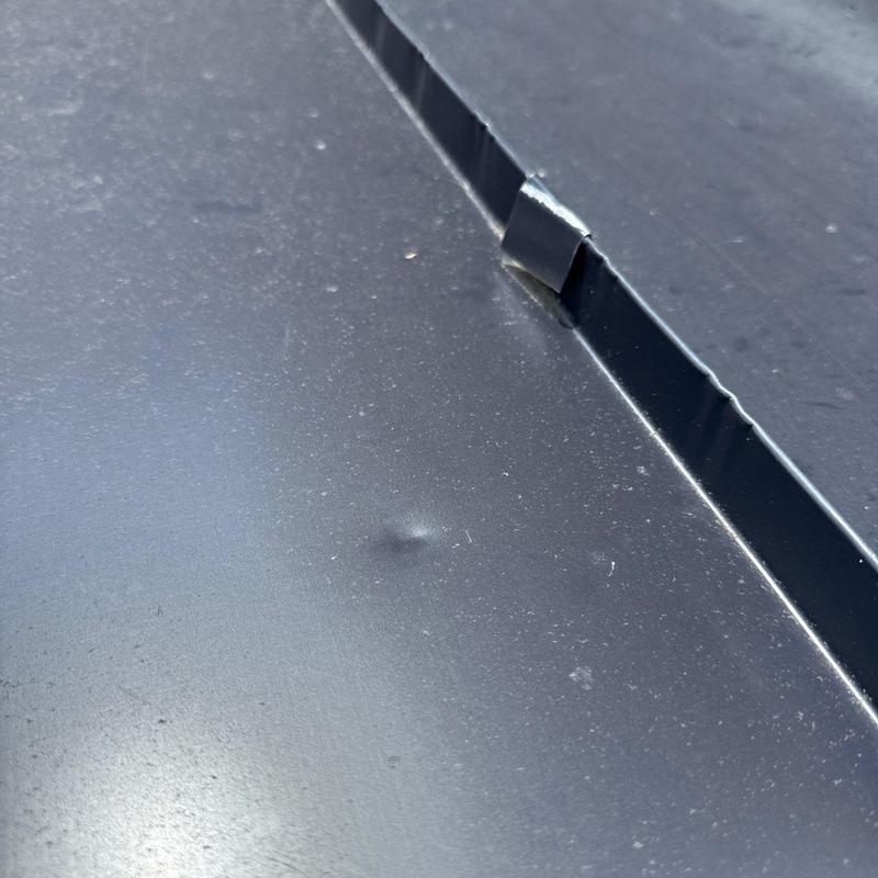 Metal roof panel with hail dent near seam