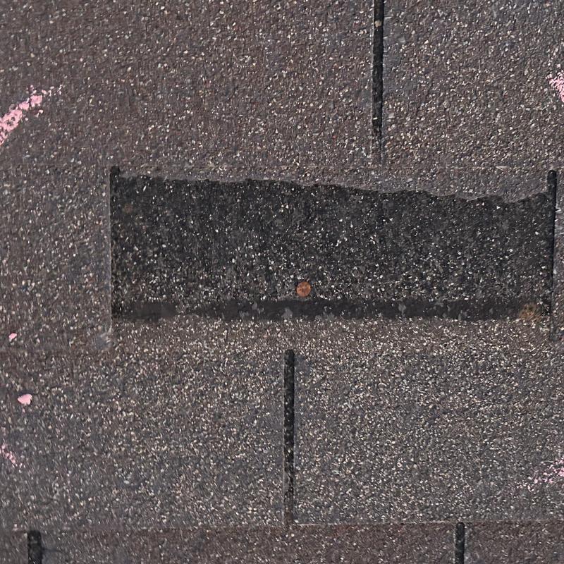 Asphalt roof shingle damage with exposed nail and markings