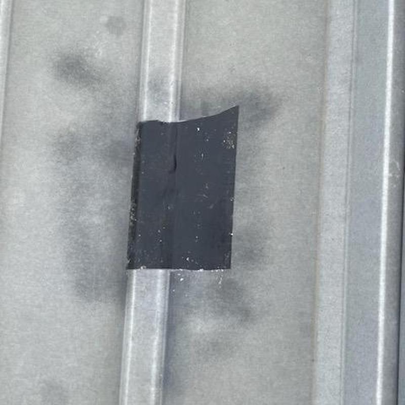 Metal storage unit roof leak patched with black tape