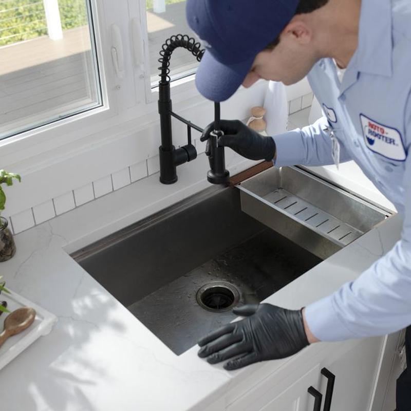 Kitchen sink drain inspection by plumber in black gloves