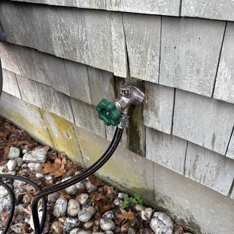 Outside faucet with green handle and hose attached