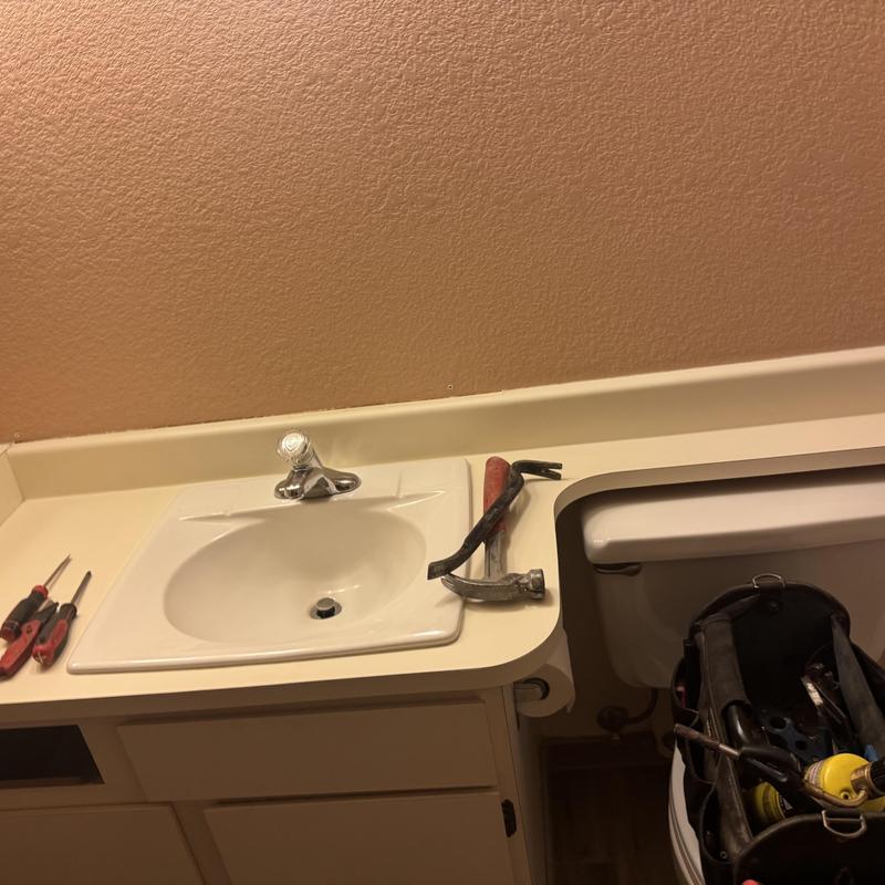 Bathroom sink and countertop with tools and toilet tank