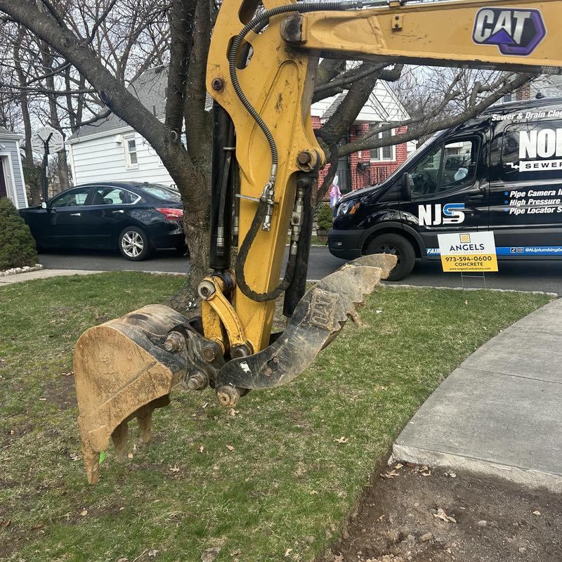 Sewer line excavation with CAT excavator bucket in yard Sewer line excavation with CAT excavator bucket in yard