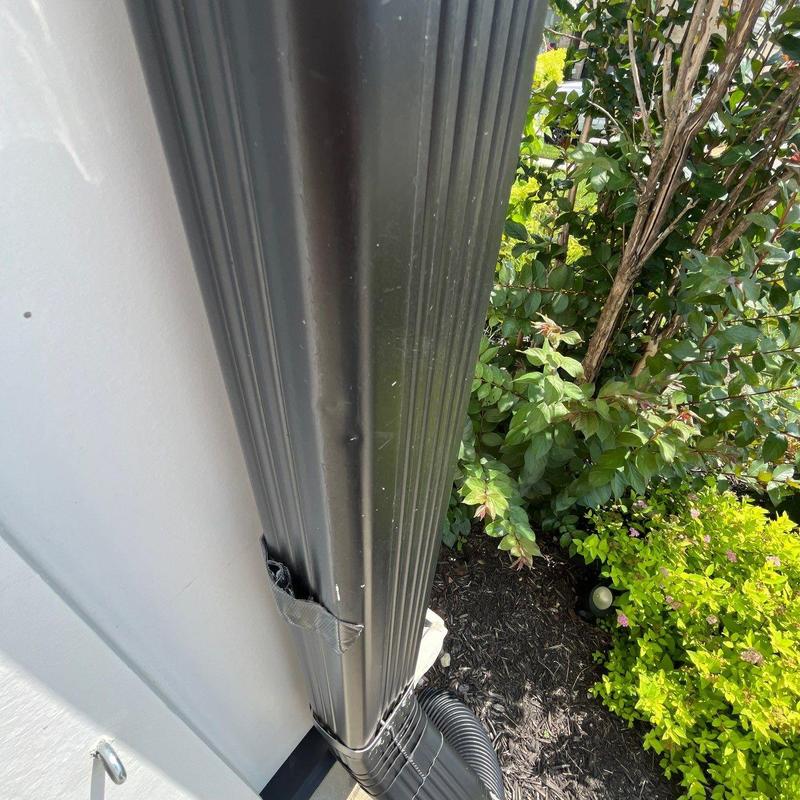 Downspout with visible dent and garden surroundings