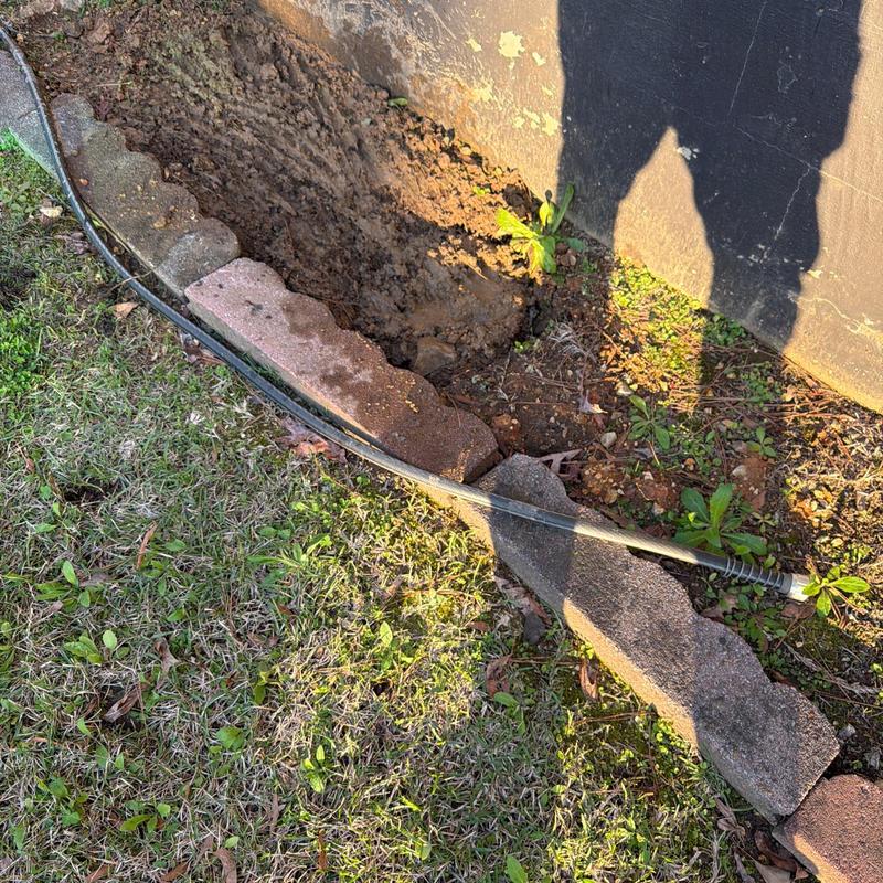 Drain cleaning hose in garden bed near house wall