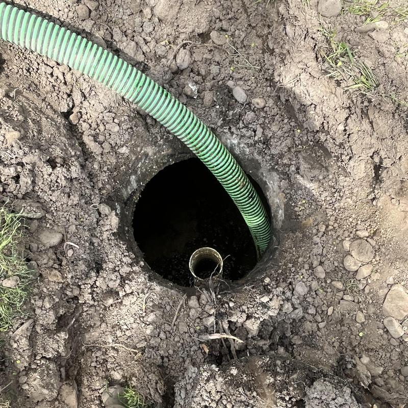 Septic tank pump-out with green suction hose in soil