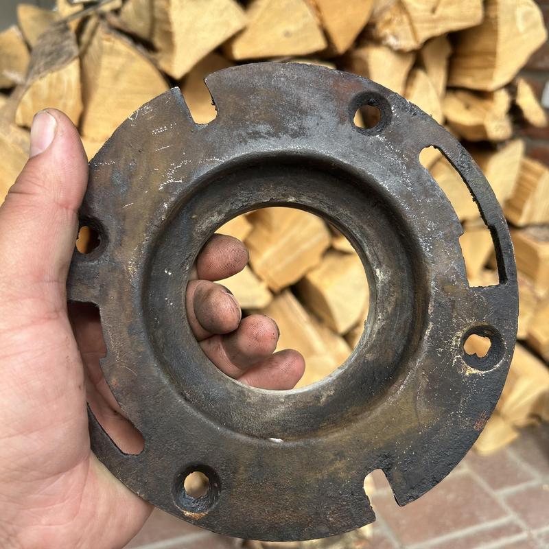 Toilet flange held in hand with wood stack background