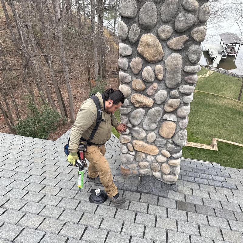 Stone chimney flashing on shingled roof with roofer working