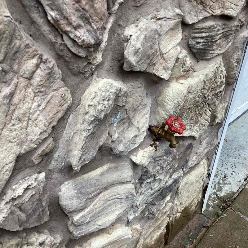 Outdoor water spigot with red handle leaking on stone wall