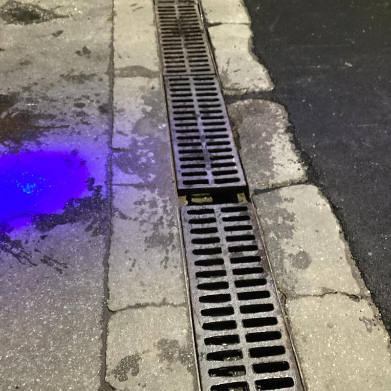 Drain grate in curbside street with water stain