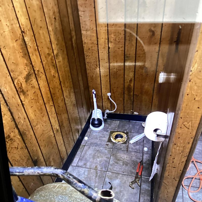 Toilet flange and plumbing inside wood-paneled bathroom stall