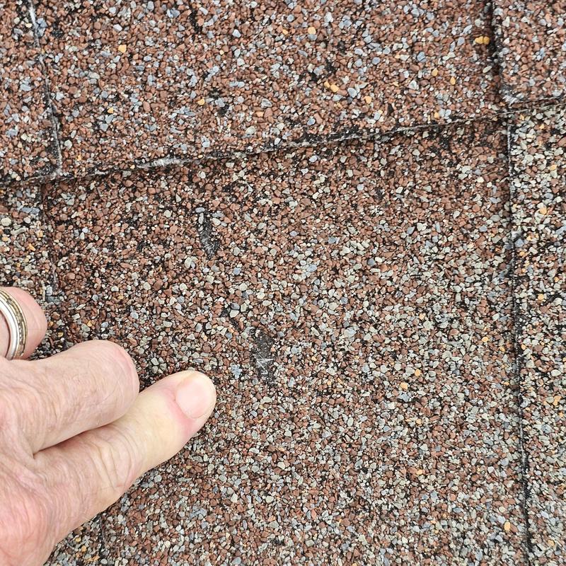 Asphalt shingle roof hail damage close-up with finger indicator