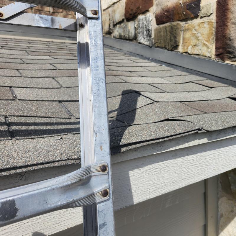 Roof shingles with visible lifting near stone wall and ladder