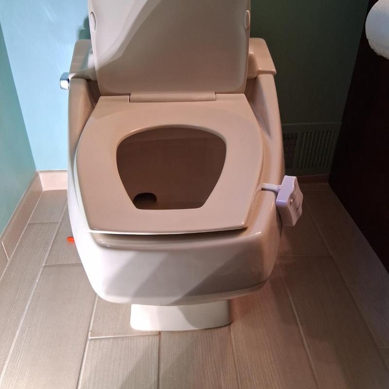 Toilet with bidet attachment in bathroom corner