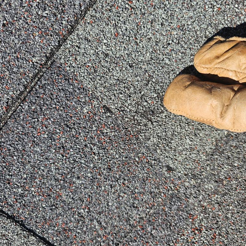 Asphalt shingle roof with hail damage close-up and glove
