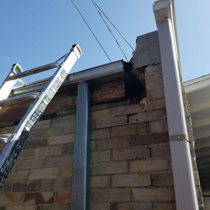 Damaged brick wall and wood beam near gutter downspout
