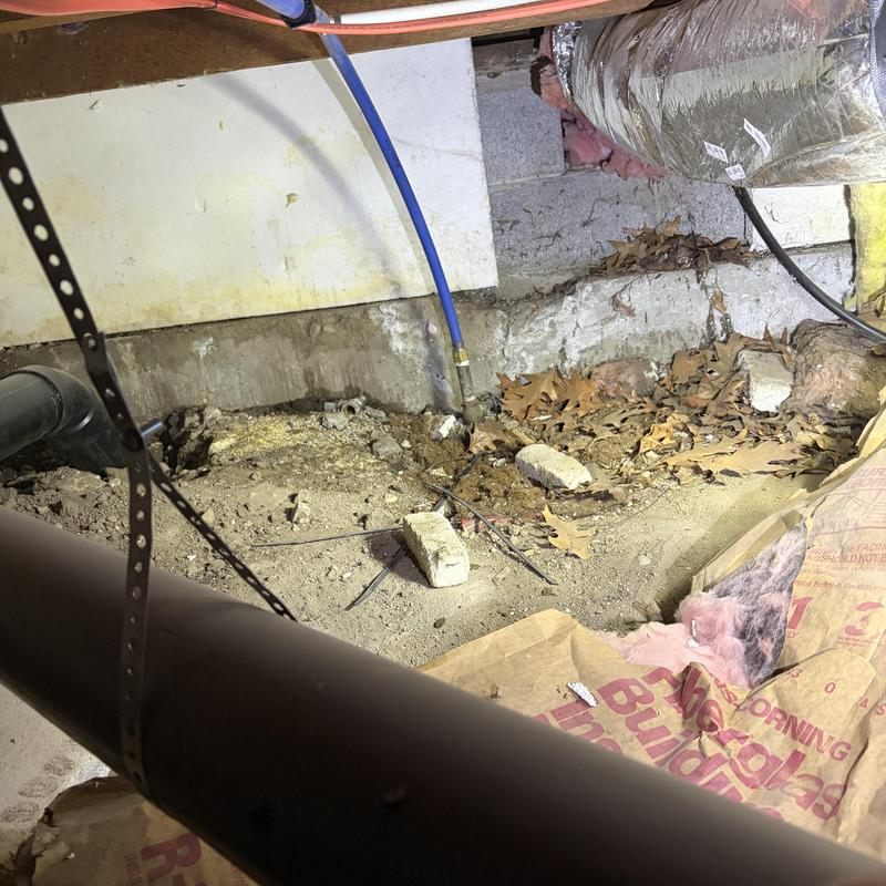 Water main pipe in crawl space with trench and debris Water main pipe in crawl space with trench and debris