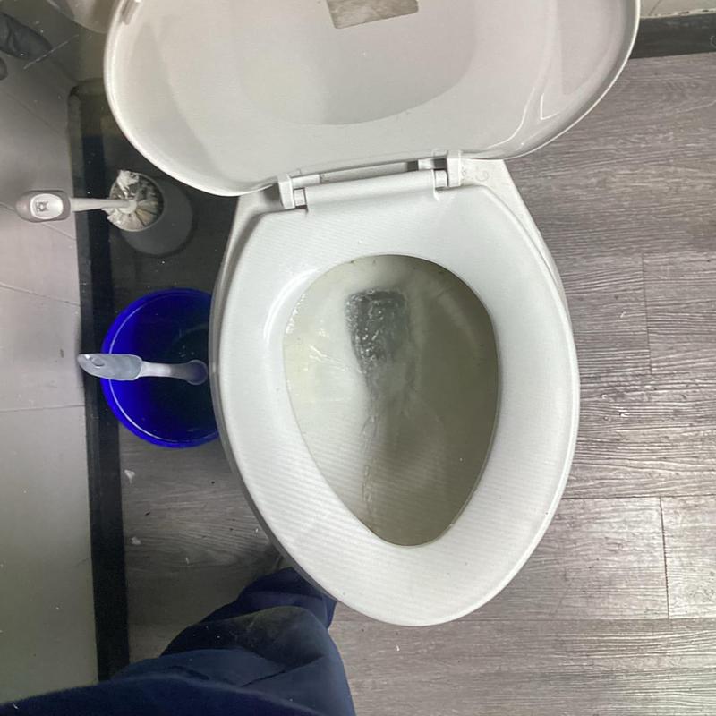 Toilet bowl flushing with open lid on bathroom floor