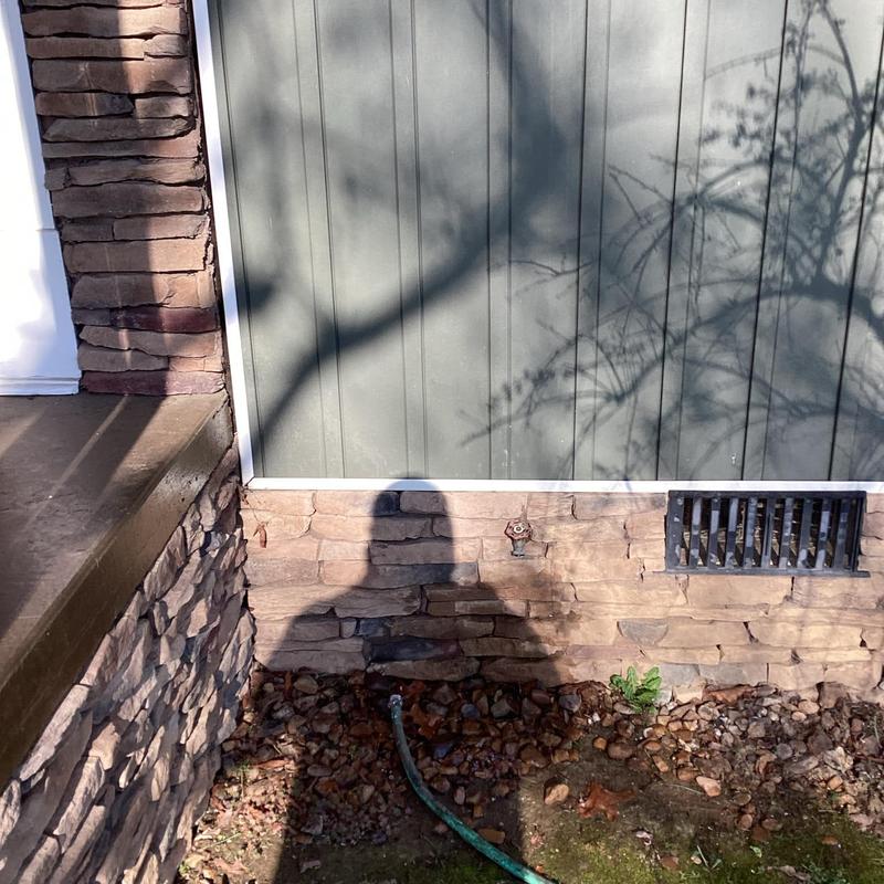 Outdoor water spigot with hose and stone wall exterior